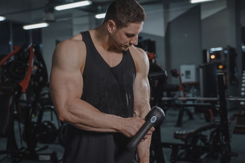 Een persoon die een massage gun gebruikt voor spierontspanning na een workout, met focus op het apparaat en de spieren.